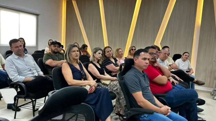 Vista da plateia durante o ato oficial. Homens e mulheres est&atilde;o sentados em cadeiras pretas de um audit&oacute;rio moderno, com pain&eacute;is de madeira e detalhes de ilumina&ccedil;&atilde;o em LED ao fundo. O p&uacute;blico acompanha atentamente os discursos sobre o investimento de mais de R$ 4 milh&otilde;es na educa&ccedil;&atilde;o inclusiva.