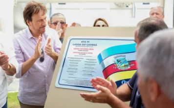 Araranguá inaugura ETA VI e amplia abastecimento de água Autoridades municipais, incluindo o prefeito César Cesa (vestindo camisa xadrez lilás à esquerda), aplaudem sorridentes diante da placa inaugural recém-descerrada da Estação de Tratamento de Água ETA VI - Lagoa do Caverá. A placa exibe o brasão de Araranguá, a data de inauguração e os nomes dos gestores municipais e vereadores. A imagem ilustra o ato oficial de entrega da obra mencionado na matéria.