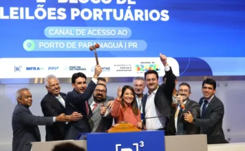 B3 bate recorde com R$ 243,8 bi em investimentos no ano Grupo de autoridades e executivos celebra no palco da B3 durante o leilão do canal de acesso ao Porto de Paranaguá. No centro da imagem, um homem ergue o martelo de madeira (gavel) simbolizando a conclusão do lance, enquanto outros sorriem e fazem sinal de "positivo". Ao fundo, um grande painel azul exibe o texto "2º Bloco de Leilões Portuários - Canal de Acesso ao Porto de Paranaguá | PR", acompanhado de logotipos institucionais do Governo Federal, Antaq e B3.