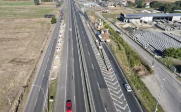 BR-101 em Maracajá terá bloqueios para novas passarelas Vista aérea da rodovia BR-101 no trecho de Maracajá (SC), exibindo as frentes de trabalho das novas passarelas nos km 401 e 402. A imagem mostra os pilares de sustentação já instalados às margens das pistas, evidenciando o local onde as vigas serão içadas pela ViaCosteira.