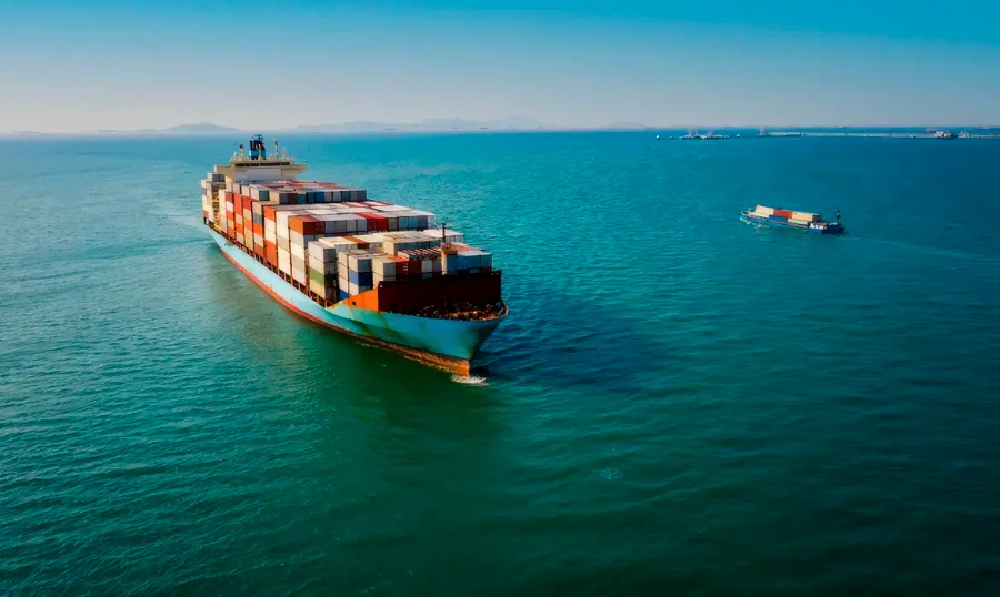 Brasil tem déficit de US$ 7,5 bi com EUA após tarifaço Grande navio porta-contêineres carregado navegando em mar aberto sob um céu limpo. A imagem ilustra o fluxo de comércio exterior e o transporte de mercadorias entre Brasil e Estados Unidos, mencionados no relatório de déficit comercial de 2025.