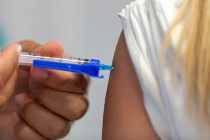 Butantan registra marcas de vacinas contra dengue e gripe Close-up de um profissional de saúde aplicando uma vacina no braço de uma pessoa vestindo camiseta branca, utilizando uma seringa com detalhe em azul.