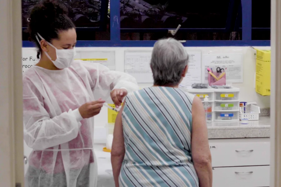 Profissional de saúde aplica vacina contra a gripe em uma mulher idosa em um ambiente clínico, ilustrando o público-alvo do novo estudo do Instituto Butantan.