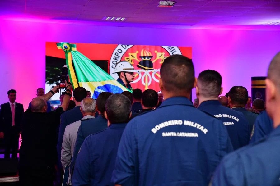 Bombeiros militares de Santa Catarina de costas, vestindo fardas azuis com a inscrição 