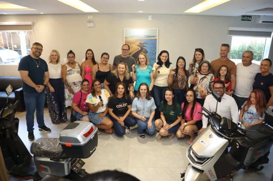 Foto oficial da entrega de prêmios da CDL Araranguá. Um grupo de pessoas, entre ganhadores e representantes da entidade, posa sorridente em uma sala ampla. Em destaque, no primeiro plano, aparecem duas scooters elétricas prateadas da campanha Natal Premiado.