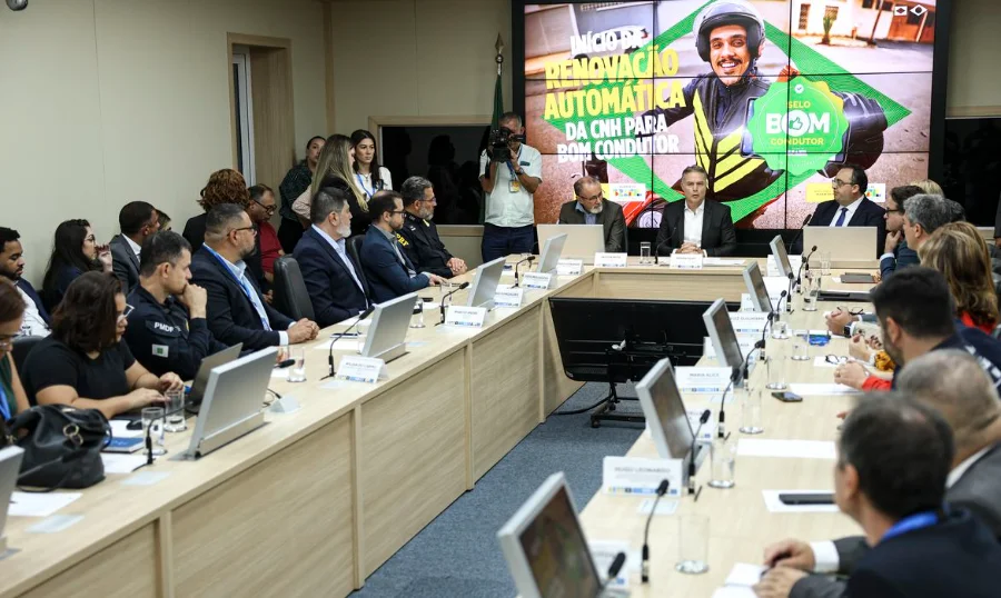 CNH automática governo libera 1º lote para bons condutores Foto de uma reunião em uma sala de conferências, onde o Ministério dos Transportes anuncia o início da renovação automática da Carteira Nacional de Habilitação (CNH) para bons condutores. Um grande telão ao fundo exibe a frase