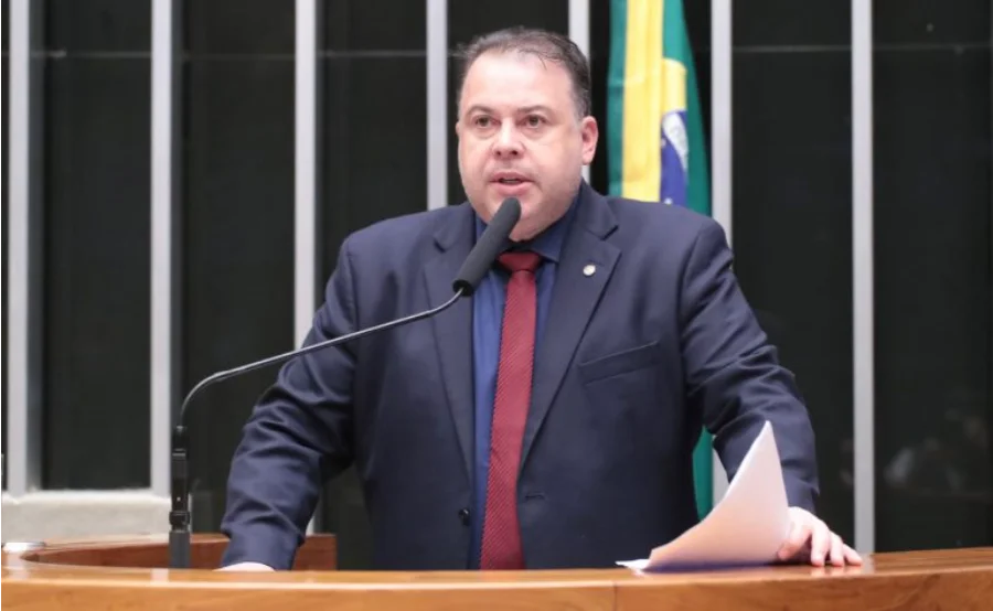 Foto do deputado federal Julio Cesar Ribeiro (Republicanos-DF), de terno escuro e gravata vermelha, falando ao microfone no púlpito da Câmara dos Deputados. Ao fundo, vê-se parte da bandeira do Brasil.
