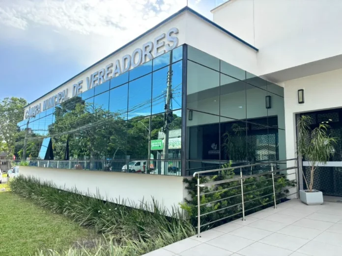 Câmara de Araranguá adota horário especial em janeiro Fachada externa do prédio moderno da Câmara Municipal de Vereadores de Araranguá, com vidros espelhados refletindo o céu e árvores.