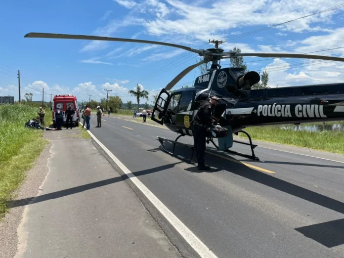 Ciclista é atropelado e fica em estado grave no Arroio do Silva Helicóptero da Polícia Civil (SAER) pousado na rodovia durante o resgate do ciclista atropelado, com equipe do SAMU e socorristas trabalhando ao fundo.