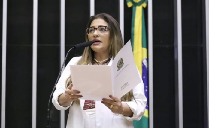 Comissão aprova prazo maior para gestantes tirarem CNH A deputada federal Ely Santos, relatora do projeto, discursa na Câmara dos Deputados segurando o parecer oficial. Ela é uma mulher de cabelos castanhos, usa óculos de grau e blazer branco. Ao fundo, vê-se parte da bandeira do Brasil. A imagem ilustra a aprovação da proposta que beneficia candidatas gestantes no processo da CNH.