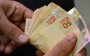 Crédito em SC prioriza capital de giro e acende alerta Mãos seguram um maço de notas de 50 reais, ilustrando recursos financeiros e o uso do dinheiro no contexto econômico de crédito e endividamento abordado na matéria.