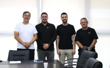 Criciúma empossa novos gestores de Obras e Comunicação Quatro homens em pé, lado a lado, sorrindo em uma sala de reuniões. O prefeito Vagner Espindola (à esquerda, de branco) e o vice Salésio Lima (à direita, de preto) ladeiam os novos gestores João Paulo Casagrande e Renan Medeiros. À frente deles, uma mesa de reuniões preta com cadeiras de escritório.