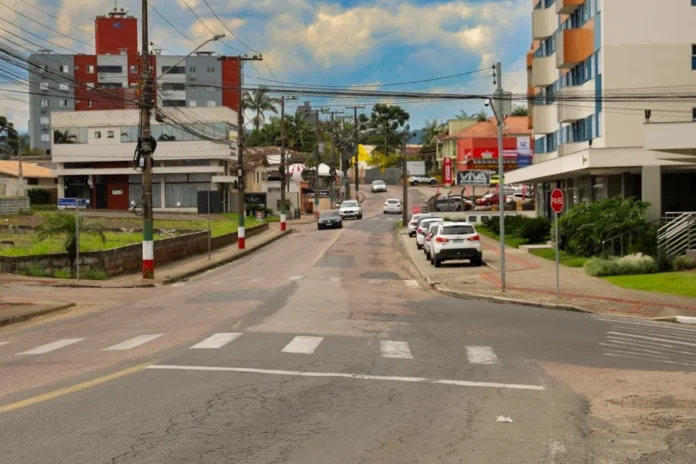 Criciúma intensifica obras no Rio Maina durante o verão Vista de uma rua no Distrito de Rio Maina, em Criciúma, que integra o pacote de obras de revitalização e melhorias na infraestrutura viária realizado pela Prefeitura Municipal. A imagem mostra o asfalto, veículos e edificações locais.