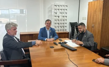 Criciúma pleiteia recursos para canal auxiliar em Brasília Foto de uma reunião em um escritório em Brasília, onde três homens estão sentados ao redor de uma grande mesa de madeira. O prefeito Vagner Espindola está entre eles, discutindo a captação de recursos para a obra do canal auxiliar de Criciúma.