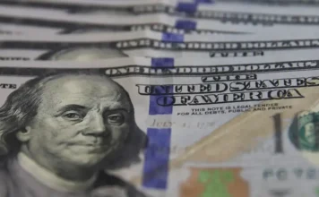 Dólar cai a R$ 5,36 e Bolsa recupera os 163 mil pontos Close de notas de cem dólares americanos em destaque, focando na efígie de Benjamin Franklin; moeda encerrou a sexta-feira em queda, cotada a R$ 5,36.
