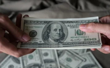 Dólar fecha a R$ 5,37 e registra quarta queda seguida Close de duas pessoas segurando um maço de notas de 100 dólares americanos. A imagem ilustra a cotação da moeda, que fechou em queda de 0,48%, vendida a R$ 5,37.