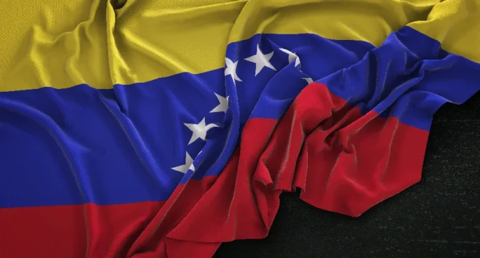 EUA apreendem petroleiros em rota para a Venezuela Close-up da bandeira da Venezuela com tecido drapeado sobre fundo preto. A imagem ilustra as tensões diplomáticas e o bloqueio econômico ao petróleo venezuelano citado na reportagem.