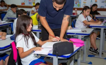 Educação de Criciúma brilha no cenário internacional Professor da rede municipal de Criciúma em sala de aula orientando uma estudante em sua carteira, ilustrando o acompanhamento pedagógico e a qualidade do ensino nas escolas municipais.
