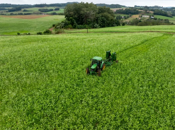 Epagri foca em agricultura digital e biotecnologia em SC Vista aérea de um trator operando em uma vasta plantação verde em Santa Catarina, ilustrando o uso de tecnologia agrícola e práticas sustentáveis no campo incentivadas pela pesquisa da Epagri.