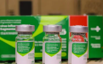 Fiocruz confirma eficácia da vacina da gripe em 2025 Fotografia em plano médio de um profissional de saúde utilizando equipamentos de proteção individual (EPIs), manuseando tubos de ensaio ou realizando análises laboratoriais. O ambiente é iluminado e sugere um laboratório de alta tecnologia, simbolizando o trabalho de vigilância genômica e monitoramento do vírus influenza realizado no Brasil.