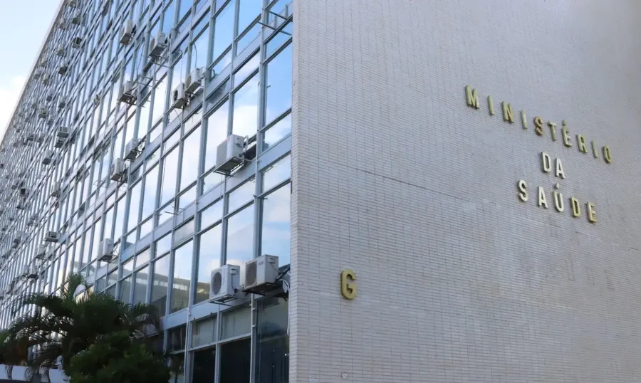 Força do SUS reforça Roraima após ataques na Venezuela Fachada lateral do edifício do Ministério da Saúde em Brasília. Em destaque, o letreiro com letras douradas sobre uma parede de pastilhas brancas. À esquerda, grandes janelas de vidro refletem o céu e exibem diversos aparelhos de ar-condicionado instalados na parte externa.