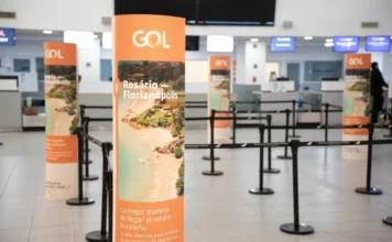 GOL lança voos diretos de Florianópolis a Córdoba e Rosário "Totens publicitários laranja da GOL Linhas Aéreas no saguão de check-in de um aeroporto, promovendo a rota 'Rosário - Florianópolis' com uma foto de praia e o texto 'La mejor manera de llegar al verano brasileño'. Organizadores de fila pretos estão dispostos em frente aos balcões de atendimento ao fundo."
