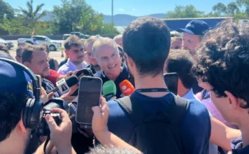 Governo anuncia túneis no Morro dos Cavalos na BR-101 O ministro dos Transportes, Renan Filho, aparece ao centro, cercado por diversos jornalistas que seguram microfones e celulares para registrar sua fala. Ele está em um ambiente aberto e ensolarado, vestindo uma camisa polo azul escura com o logotipo do Ministério dos Transportes, durante o anúncio das obras de construção dos túneis no Morro dos Cavalos, na BR-101.