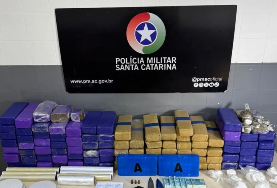 Apreensão de mais de 70 kg de drogas, balanças e munições dispostas sobre mesa branca em unidade da Polícia Militar.