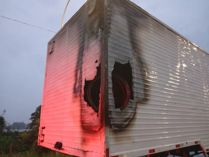 Incêndio atinge carga de caminhão em Passo de Torres Baú de carreta branca com danos visíveis de incêndio, incluindo furos e marcas de queimado na lateral e traseira, após ocorrência na BR-101 em Passo de Torres.