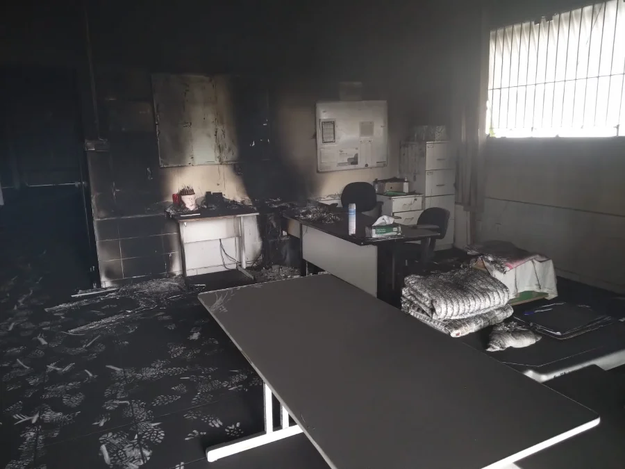 Vista geral da recepção do Centro Pop em Criciúma com paredes e chão cobertos de fuligem preta após o incêndio. Móveis de escritório danificados são visíveis ao fundo.