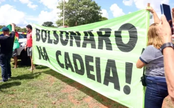 Juristas alertam para riscos de anistia a golpistas do 8/1 Manifestantes seguram uma grande faixa de cor verde-limão com a frase "BOLSONARO NA CADEIA!" escrita em letras garrafais pretas. Ao fundo, é possível ver parte da bandeira do Brasil e pessoas acompanhando o ato ao ar livre, simbolizando o pedido de responsabilização citado na matéria.