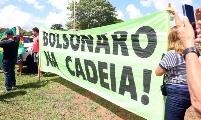 Juristas alertam para riscos de anistia a golpistas do 8 1 Manifestantes seguram uma grande faixa de cor verde-limão com a frase "BOLSONARO NA CADEIA!" escrita em letras garrafais pretas. Ao fundo, é possível ver parte da bandeira do Brasil e pessoas acompanhando o ato ao ar livre, simbolizando o pedido de responsabilização citado na matéria.