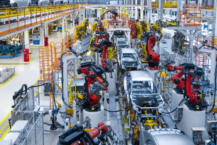 Juros altos travam crédito para 80% da indústria Linha de montagem de fábrica de automóveis com múltiplos robôs industriais vermelhos trabalhando em carrocerias de carros. A imagem ilustra o setor industrial que, segundo pesquisa da CNI citada na matéria, enfrenta dificuldades de acesso a crédito e juros elevados, o que pode frear investimentos em automação e expansão como os mostrados.