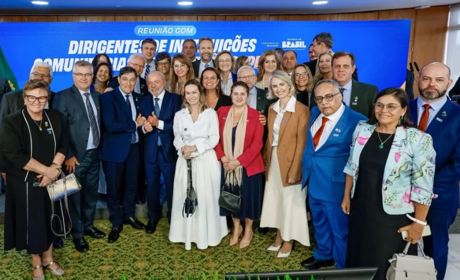 Foto em grupo do presidente Luiz Inácio Lula da Silva com diversos dirigentes de instituições comunitárias de educação superior, posando em frente a um banner oficial do evento em Brasília.