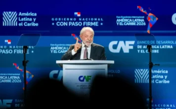 Lula defende união da América Latina e Caribe no Panamá Fotografia do presidente Luiz Inácio Lula da Silva discursando em um púlpito branco com o logotipo do Banco de Desenvolvimento da América Latina (CAF). Ele veste terno escuro e gravata, gesticulando com o dedo indicador da mão direita para enfatizar seu discurso. Ao fundo, painéis azuis exibem as marcas do "Fórum Econômico Internacional – América Latina e Caribe 2026" e do governo do Panamá.