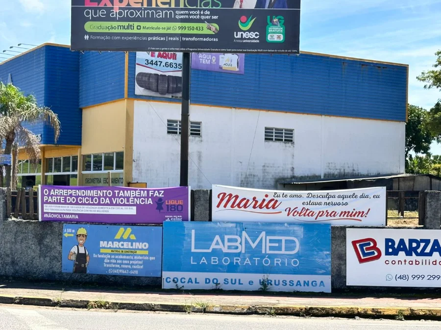 Faixas da campanha contra violência doméstica em Cocal do Sul fixadas em muro: ao lado de um pedido de desculpas escrito 'Maria, volta pra mim', um aviso roxo alerta que o arrependimento faz parte do ciclo da violência.