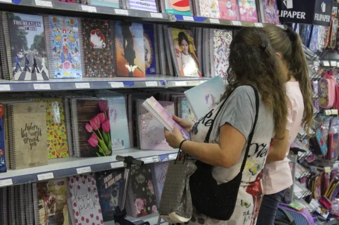 Material escolar tem variação de até 253% em Criciúma Consumidoras pesquisam cadernos em uma papelaria, ilustrando a busca por material escolar mencionada na matéria sobre a grande variação de preços encontrada pelo Procon de Criciúma.
