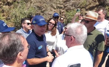Ministro vistoria obras da BR-285 em Timbé do Sul O ministro dos Transportes, Renan Filho, usando um boné azul do ministério, conversa com o prefeito de Timbé do Sul, Vilmar Maffiolette, e outras autoridades regionais. Eles estão em uma área externa de obras na Serra da Rocinha, com uma encosta rochosa protegida por telas metálicas ao fundo. O grupo está em círculo, atento à fala do ministro.