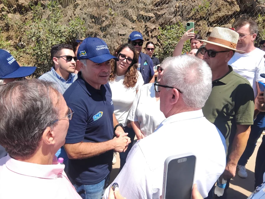 Ministro vistoria obras da BR-285 em Timbé do Sul O ministro dos Transportes, Renan Filho, usando um boné azul do ministério, conversa com o prefeito de Timbé do Sul, Vilmar Maffiolette, e outras autoridades regionais. Eles estão em uma área externa de obras na Serra da Rocinha, com uma encosta rochosa protegida por telas metálicas ao fundo. O grupo está em círculo, atento à fala do ministro.