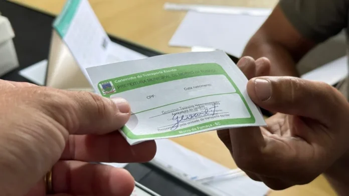 Morro da Fumaça inicia emissão de carteirinhas escolares Mãos aparecem em close segurando a carteirinha de transporte escolar da Prefeitura Municipal de Morro da Fumaça, um cartão branco com detalhes em verde. O documento, cuja confecção para 2026 é tema da matéria, é obrigatório para o uso do transporte gratuito por estudantes no município.