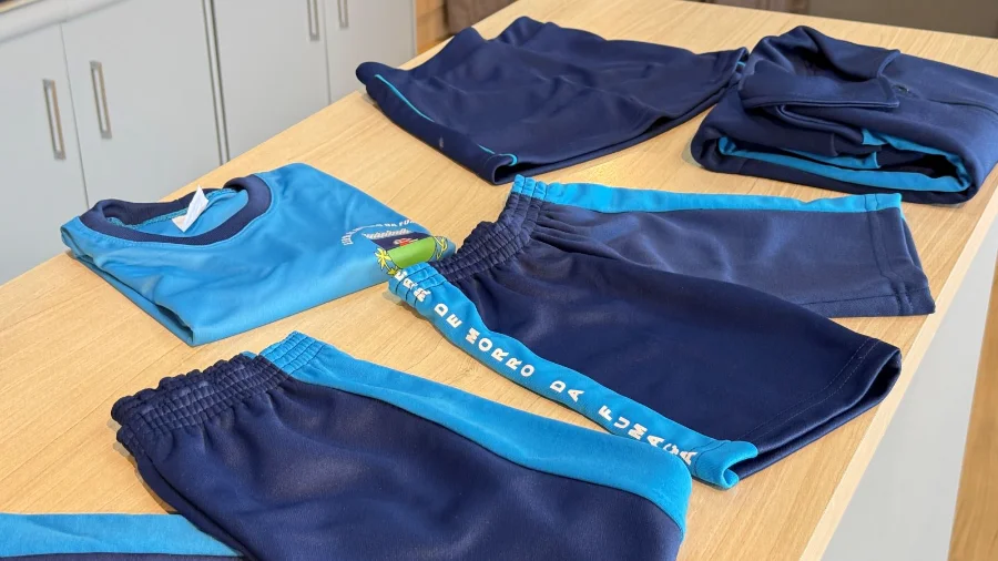 Conjunto de peças do uniforme escolar da Rede Municipal de Ensino de Morro da Fumaça, nas cores azul e azul-marinho, dispostas sobre uma mesa.