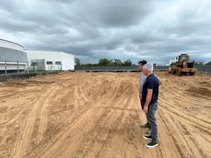 Obras do estacionamento da Câmara avançam em Araranguá "Presidente da Câmara de Vereadores de Araranguá, Paulinho Souza, vistoria o canteiro de obras do novo estacionamento da Casa Legislativa, atualmente em fase de terraplanagem. Ao fundo, observa-se o prédio da Câmara e um trator."