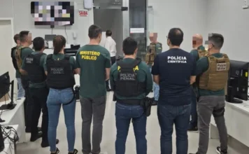 Operação Aurantium apura uso de laranjas em Criciúma Foto mostra, de costas, um grupo de agentes das forças de segurança que integram o GAECO reunidos em uma sala durante a deflagração da Operação Aurantium. É possível identificar, pelos uniformes, membros da Polícia Civil, do Ministério Público, da Polícia Penal e da Polícia Científica, ilustrando a composição da força-tarefa responsável pela investigação.