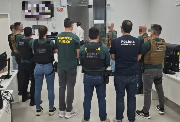 Operação Aurantium apura uso de laranjas em Criciúma Foto mostra, de costas, um grupo de agentes das forças de segurança que integram o GAECO reunidos em uma sala durante a deflagração da Operação Aurantium. É possível identificar, pelos uniformes, membros da Polícia Civil, do Ministério Público, da Polícia Penal e da Polícia Científica, ilustrando a composição da força-tarefa responsável pela investigação.