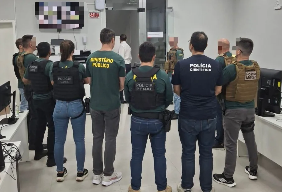 Foto mostra, de costas, um grupo de agentes das forças de segurança que integram o GAECO reunidos em uma sala durante a deflagração da Operação Aurantium. É possível identificar, pelos uniformes, membros da Polícia Civil, do Ministério Público, da Polícia Penal e da Polícia Científica, ilustrando a composição da força-tarefa responsável pela investigação.