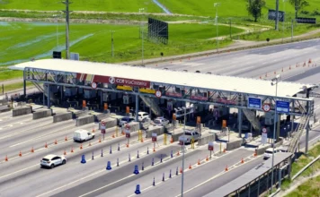 Pedágio na BR-101: saiba como evitar filas no verão Vista aérea de uma praça de pedágio da ViaCosteira na BR-101 Sul, sob luz do dia, mostrando diversas pistas com fluxo de veículos. Pistas exclusivas para cobrança automática estão sinalizadas, ilustrando as alternativas para evitar filas durante viagens de verão.