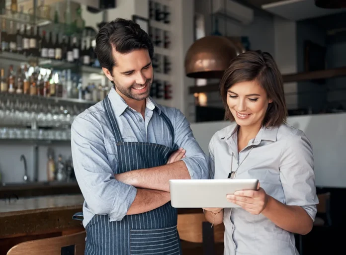 Pequenos negócios geram 60,5% dos empregos em SC Casal de empreendedores em seu estabelecimento analisando tablet, ilustrando a liderança das micro e pequenas empresas na geração de empregos em Santa Catarina segundo o Sebrae.