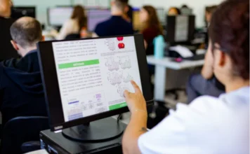 Pós-graduação da Unesc cresce em avaliação nacional Pesquisador em laboratório de informática da Unesc aponta para tela de computador exibindo gráficos e dados científicos, ilustrando o trabalho de pesquisa e a qualidade dos programas de pós-graduação da instituição, reconhecidos na avaliação da Capes.