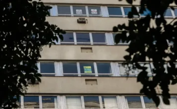 Receita nega novo imposto para aluguel de temporada Fachada de um edifício residencial com diversas janelas, algumas exibindo placas de "Aluga-se" e "Vende-se". A imagem ilustra o mercado de locação de imóveis no Brasil, foco das recentes clarificações da Receita Federal sobre a tributação de aluguéis por temporada.