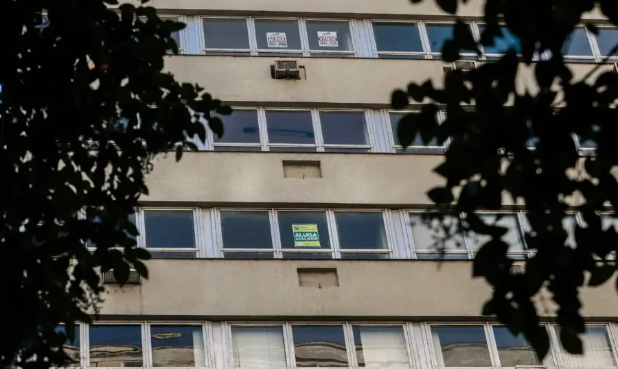 Fachada de um edifício residencial com diversas janelas, algumas exibindo placas de 